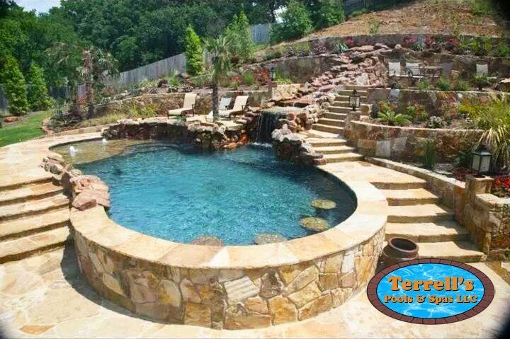 A large swimming pool surrounded by rocks and stairs in a backyard.