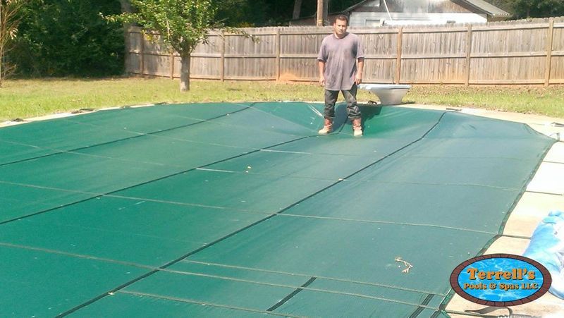 A man is standing on top of a green pool cover.