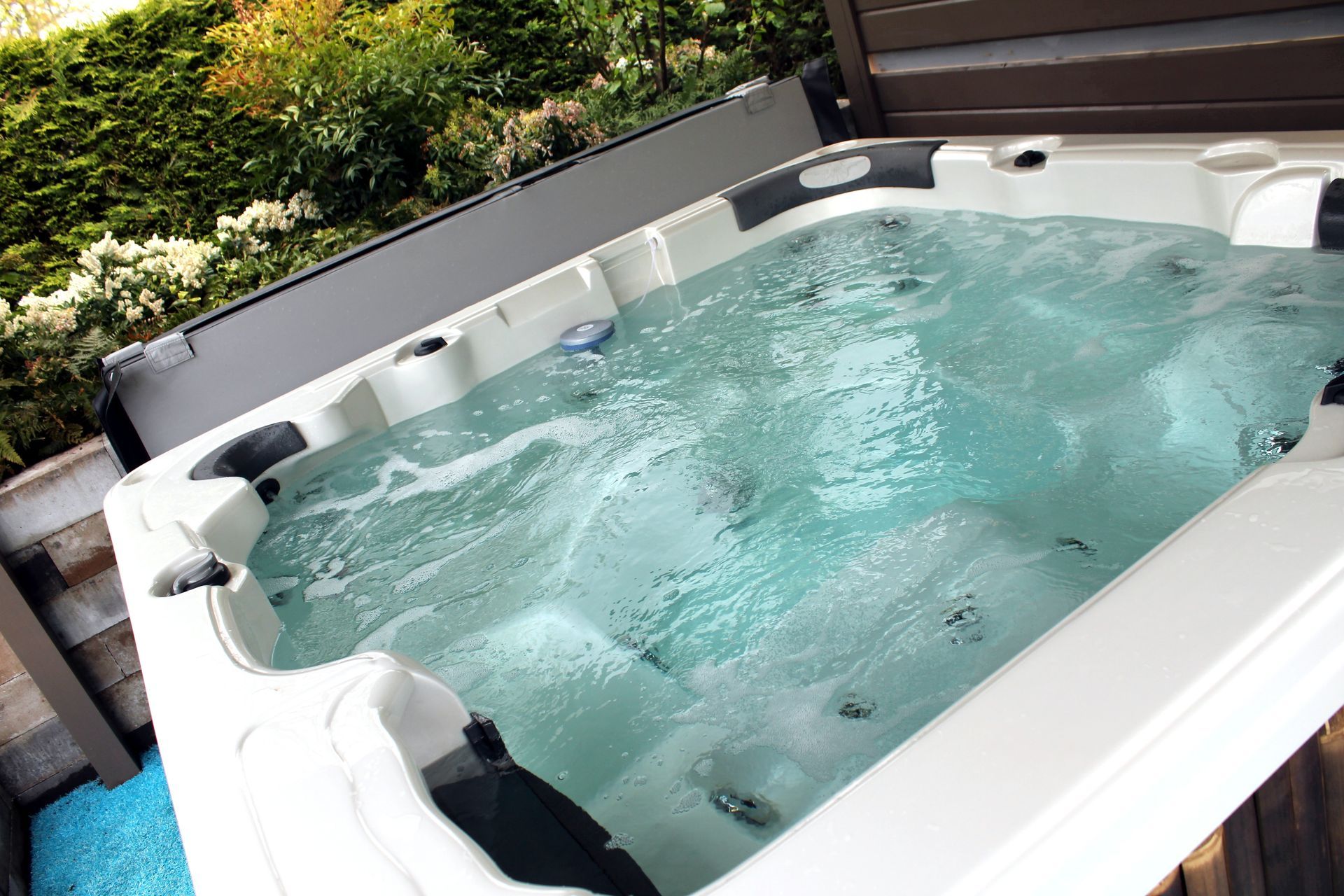 A white hot tub filled with blue water is sitting on a wooden deck.