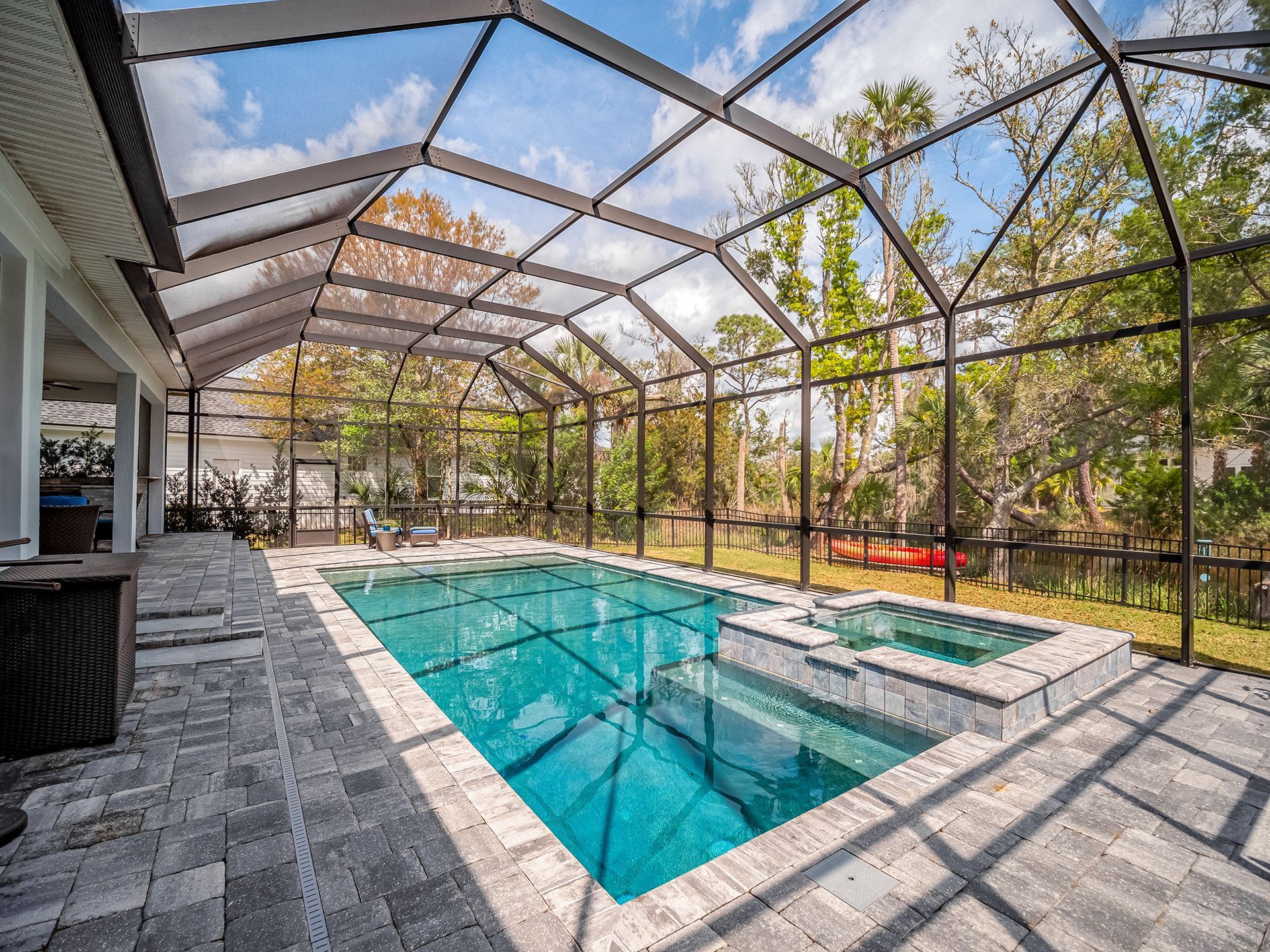 There is a large swimming pool in the backyard of a house with a screened in area.