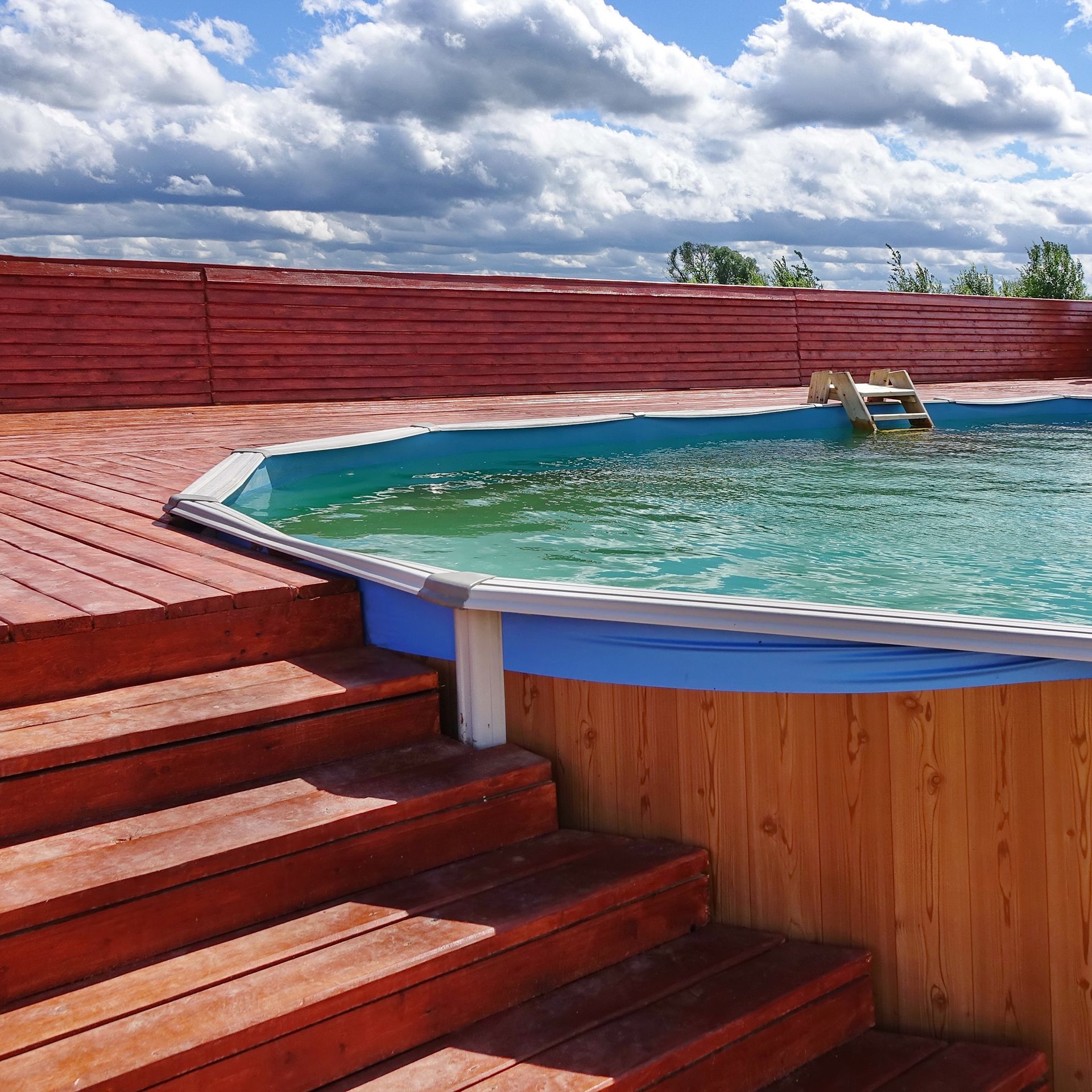 A swimming pool surrounded by wooden steps and a red fence