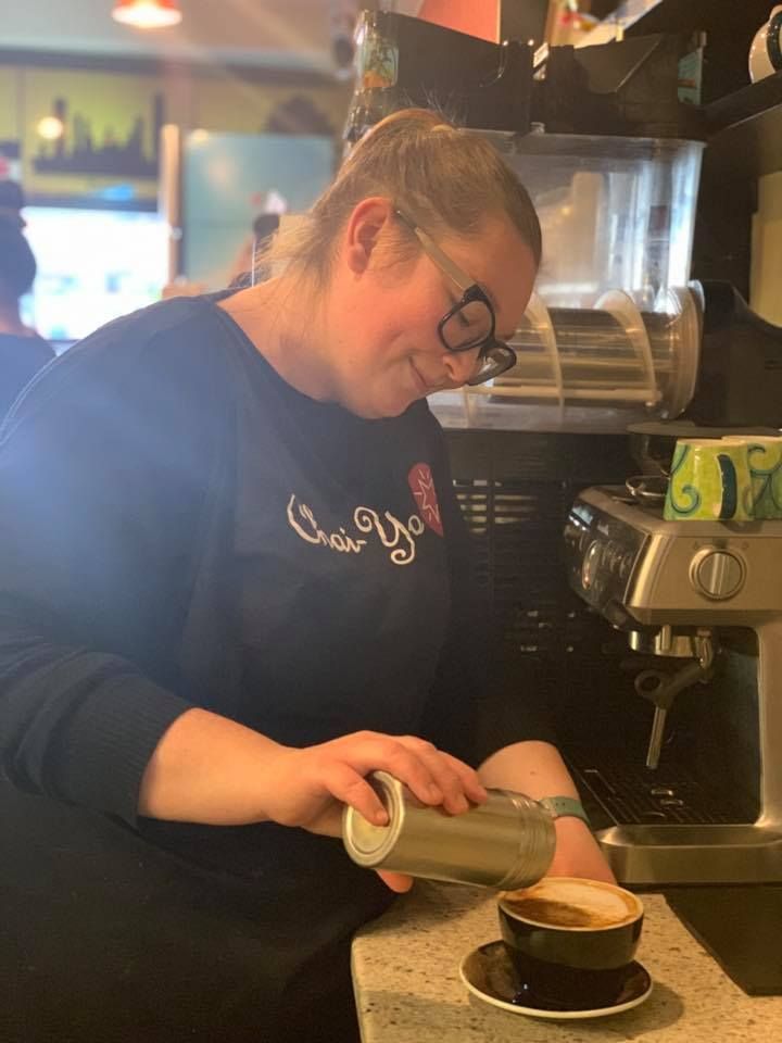 A woman is pouring milk into a cup of coffee.