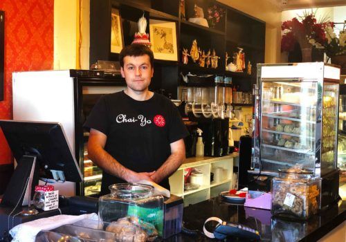 A man standing behind a counter wearing a shirt that says chai you