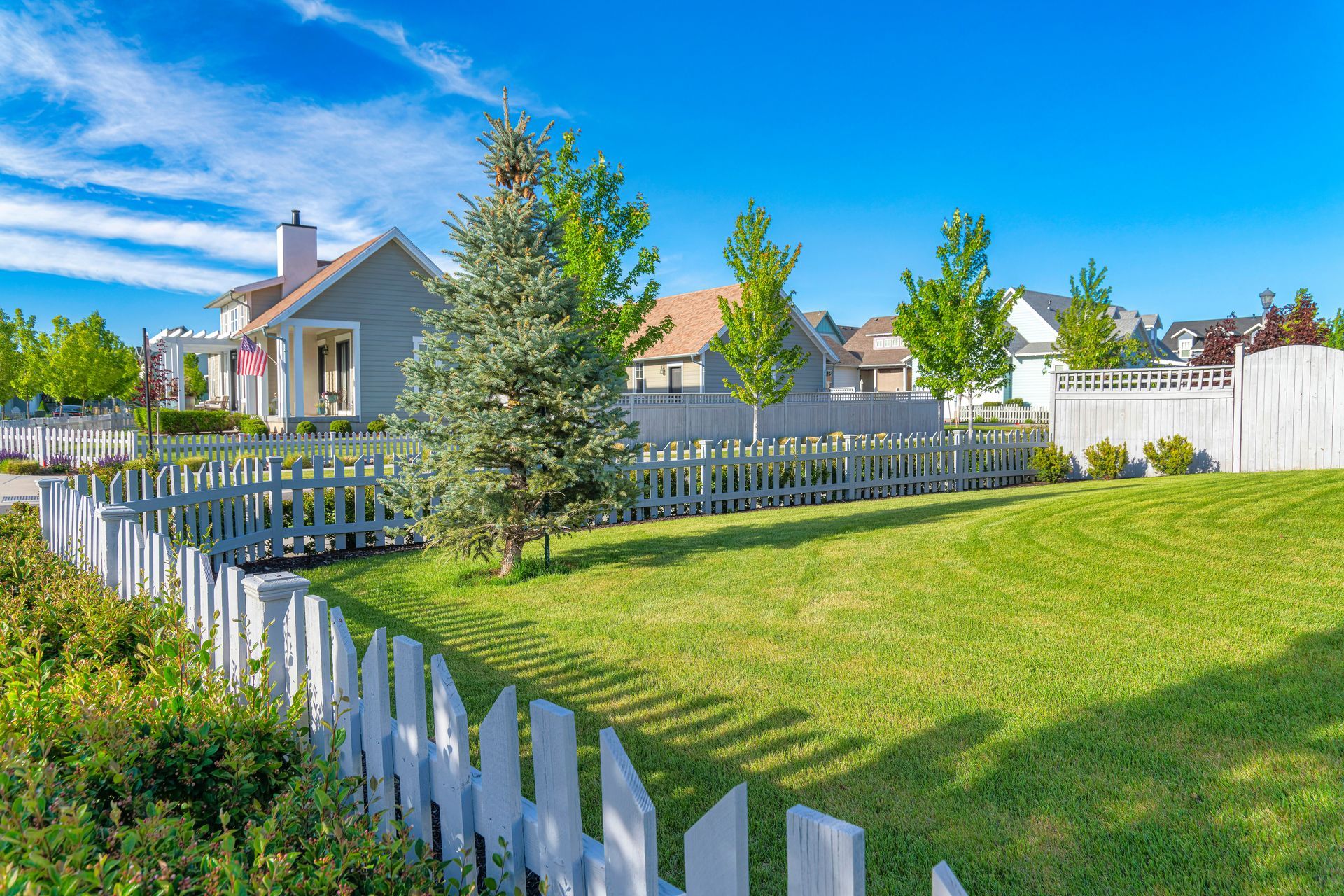 A white picket fence surrounds a lush green lawn in front of a house.