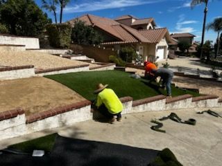 Two men are installing artificial grass in front of a house.