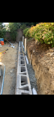 A concrete block wall is being built on top of a dirt hill.