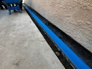 A blue chair is sitting next to a blue pipe on the side of a building.