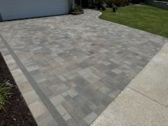 A brick driveway leading to a garage and a lush green lawn.