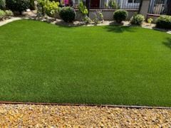 A lush green lawn with a gravel border in front of a house.