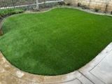 A lush green lawn with a patio in the background.