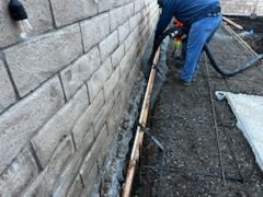 A man is pouring concrete into a hole next to a brick wall.