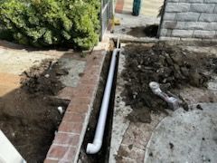 A pipe is being installed in a trench next to a brick wall.