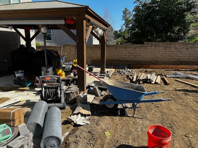 A wheelbarrow is sitting in the dirt next to a red bucket.