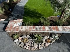 A brick wall is surrounded by rocks and plants in a garden.