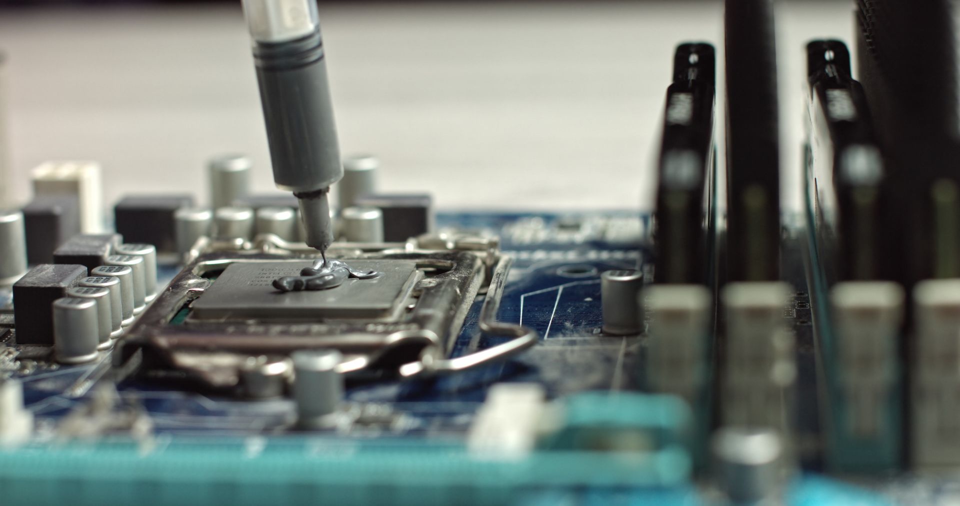 Applying thermal paste to a CPU on a motherboard, using a syringe.