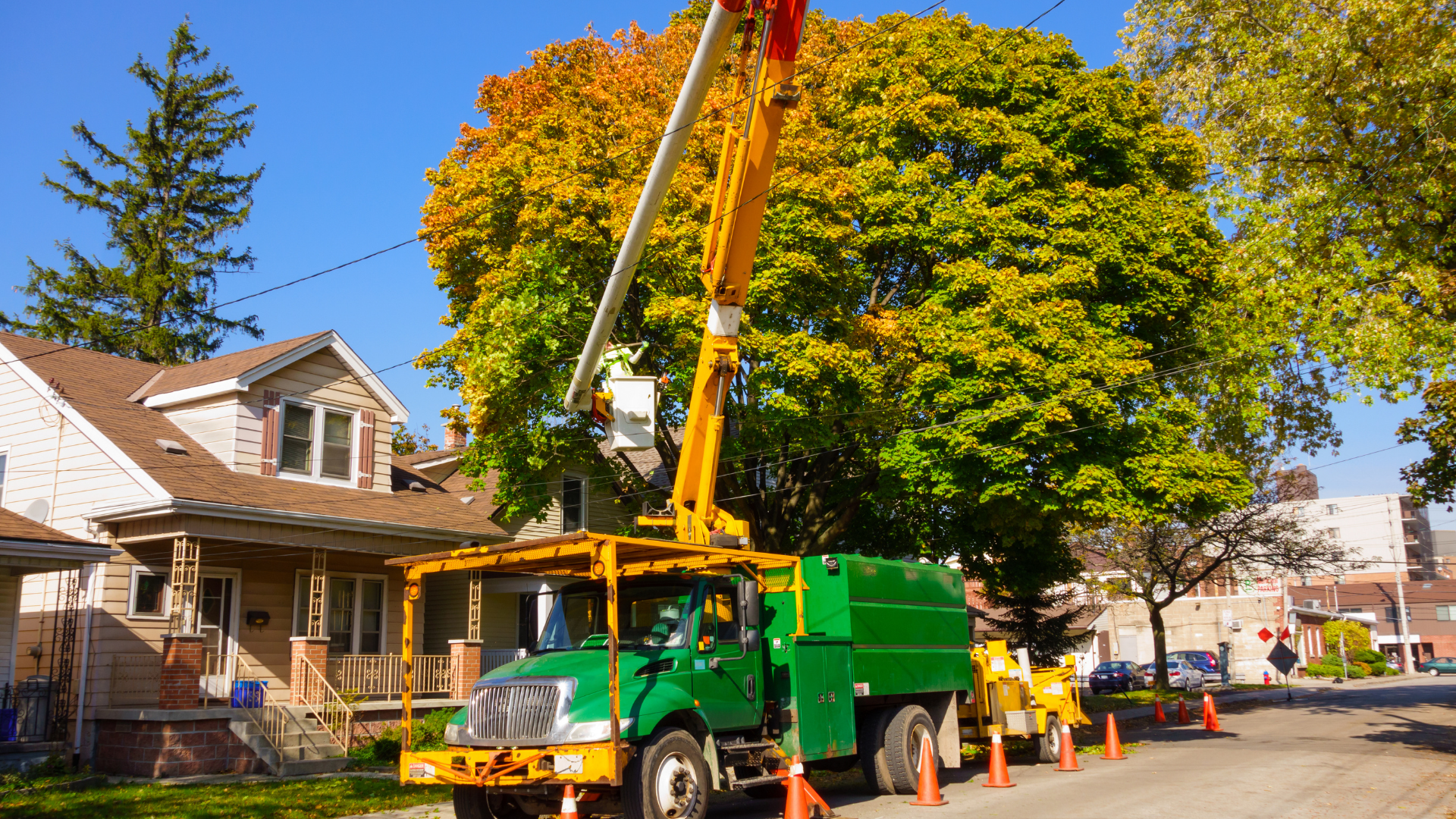 A green and yellow tree trimming truck is parked in front of a house.