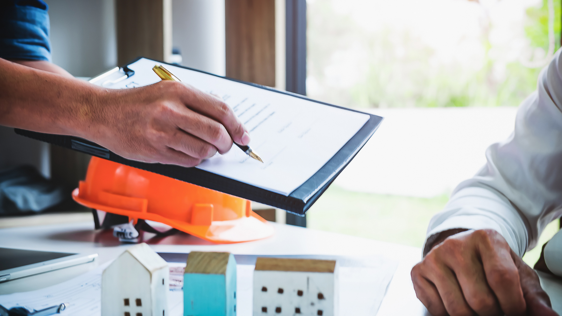 A man is writing on a clipboard while another man looks on.