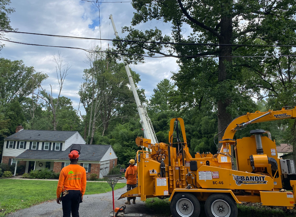 A man is standing next to a tree chipper in front of a house.