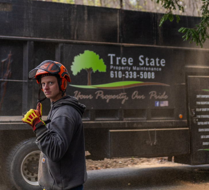 A man wearing a helmet stands in front of a tree state truck