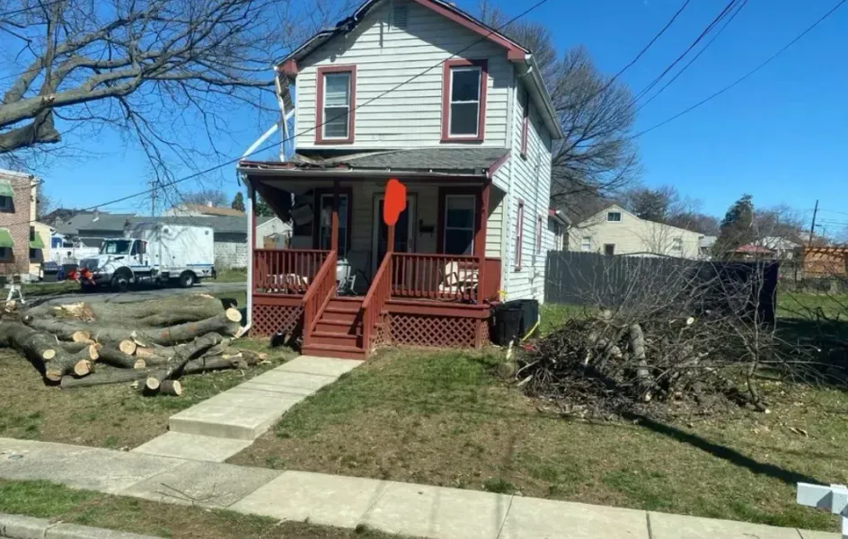 A white house with a red porch is sitting next to a pile of logs.