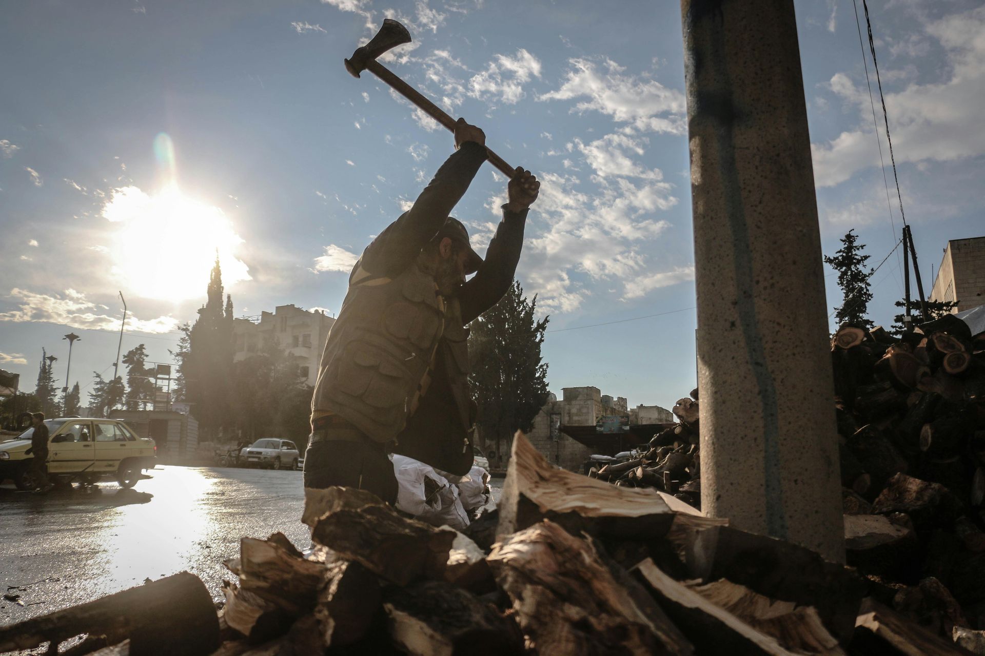 Man chops wood with an ax outdoors, sunlight shines in the background.