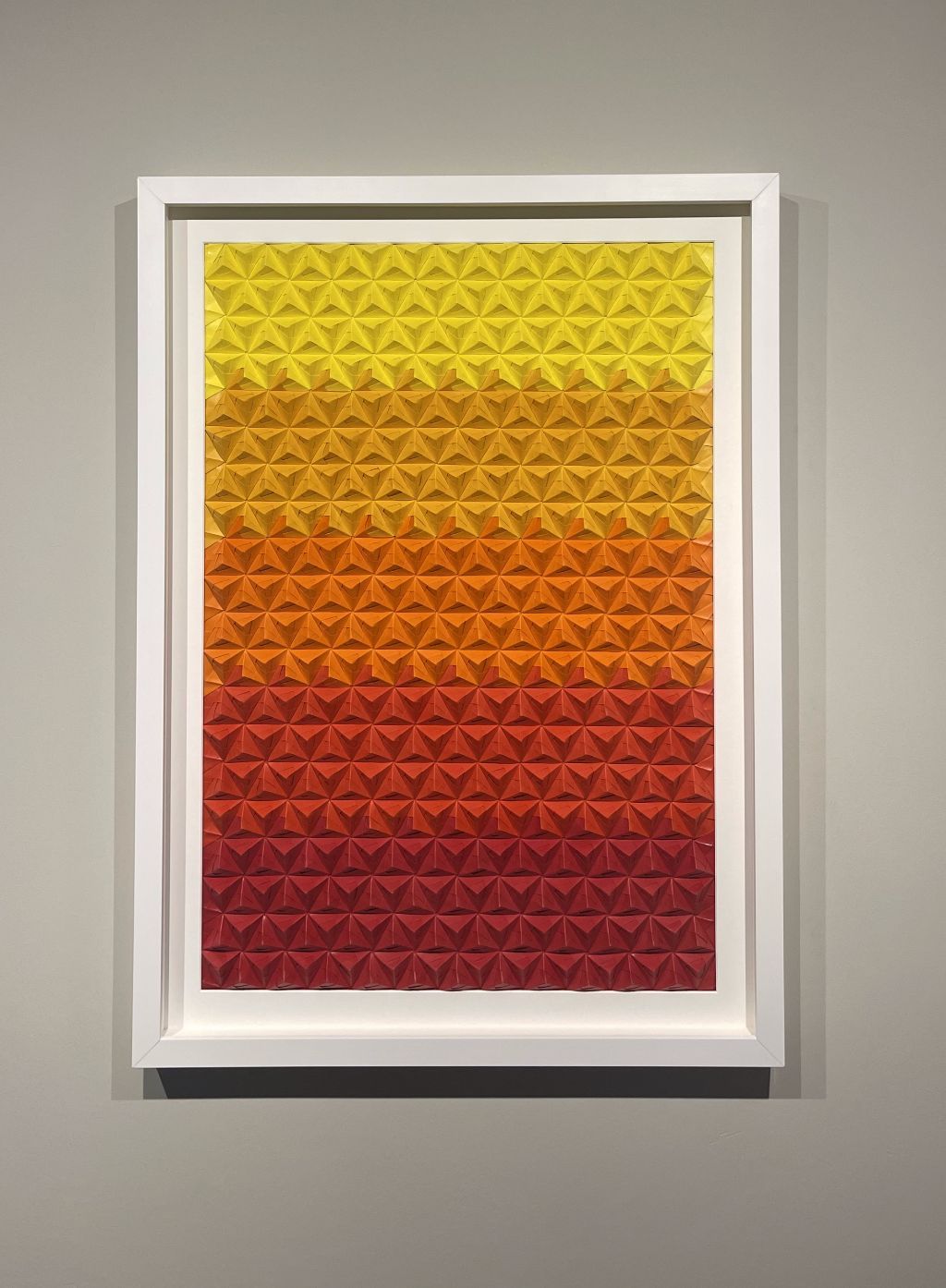 A framed painting of yellow and red triangles on a wall