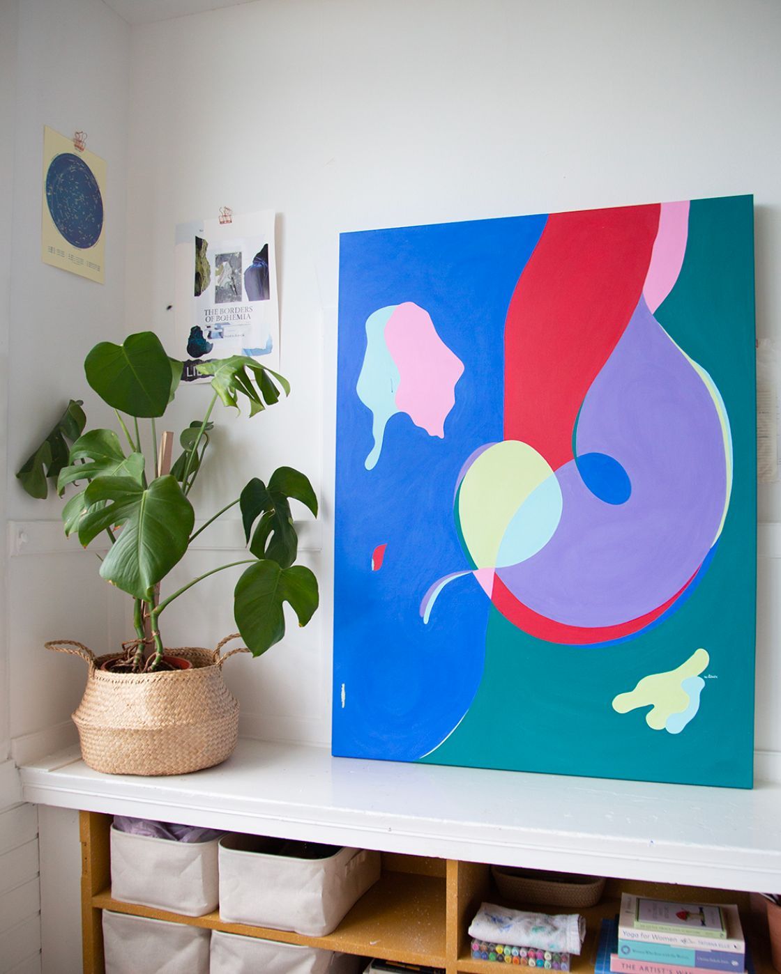 A colorful painting is hanging on a wall next to a potted plant