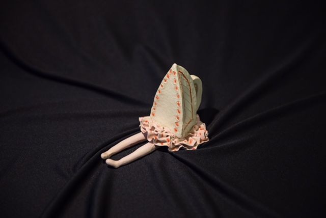 A doll is laying on a black cloth with an iron on her head