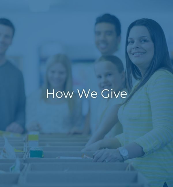 Group of people sitting at a conference table with the text “How We Give” overlaid in blue tint