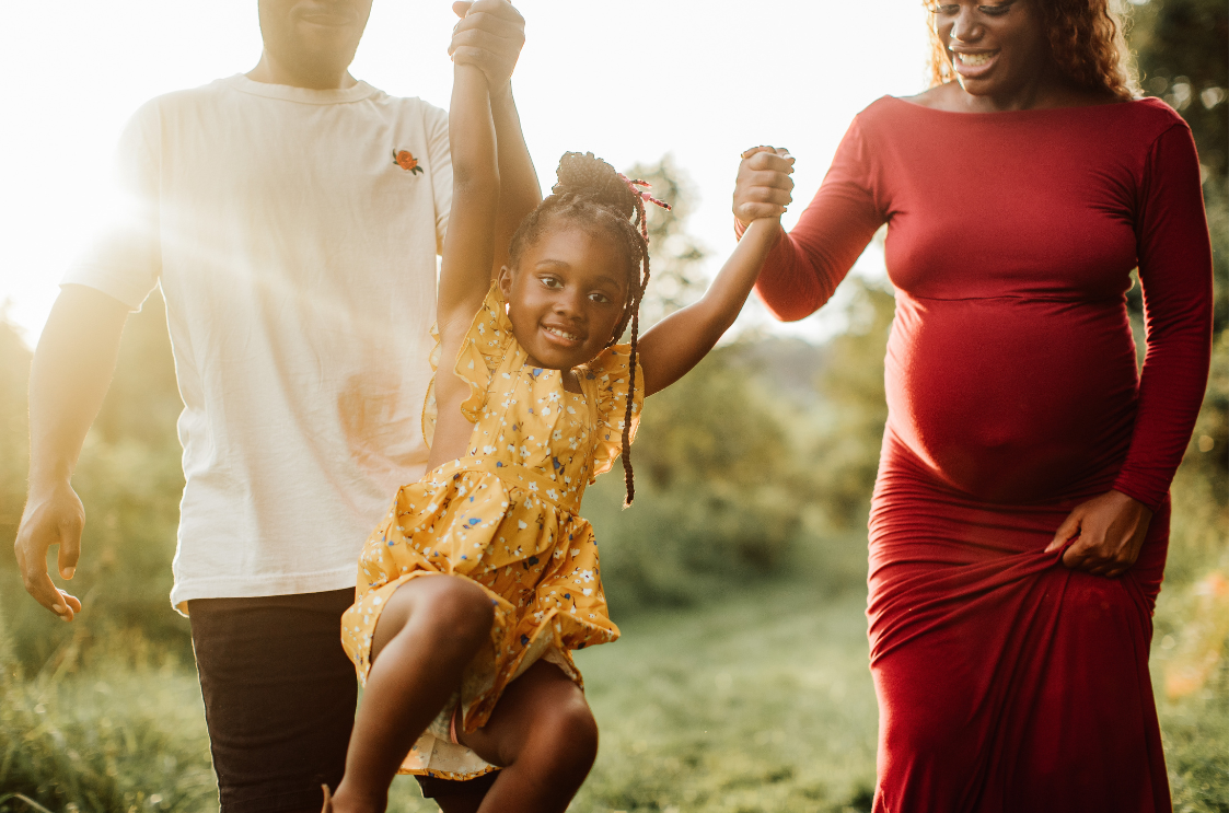 A pregnant woman is holding a little girl 's hand while walking with her husband and daughter.