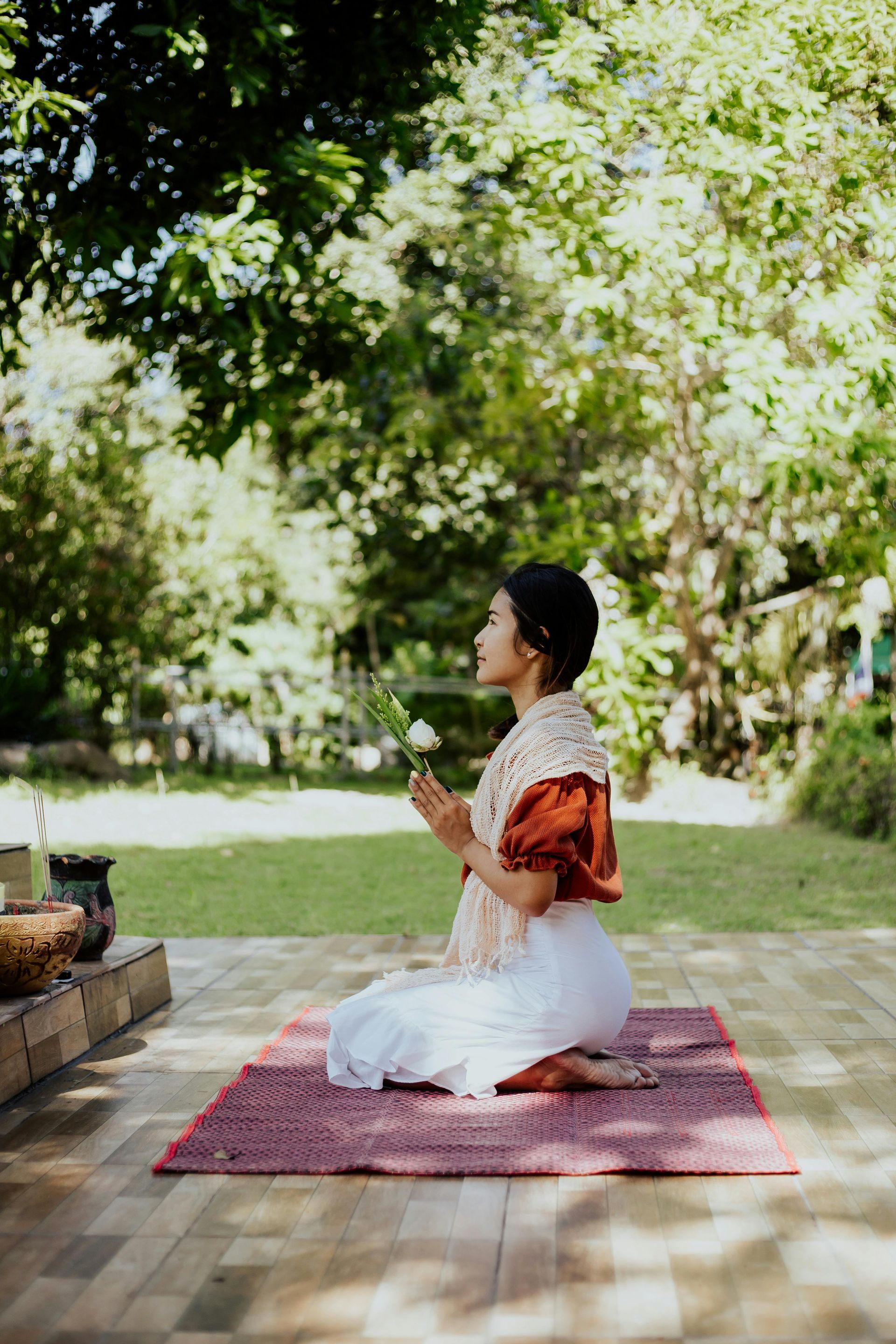 A woman is kneeling on a yoga mat in a park.