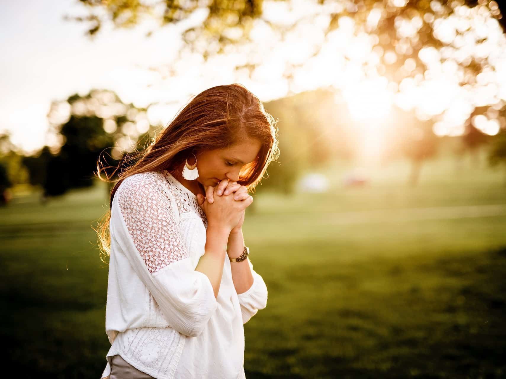 A woman is praying in a park with her hands folded.