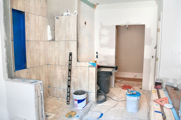 Bagno in costruzione; piastrelle beige in fase di installazione, impermeabilizzazione blu visibile.
