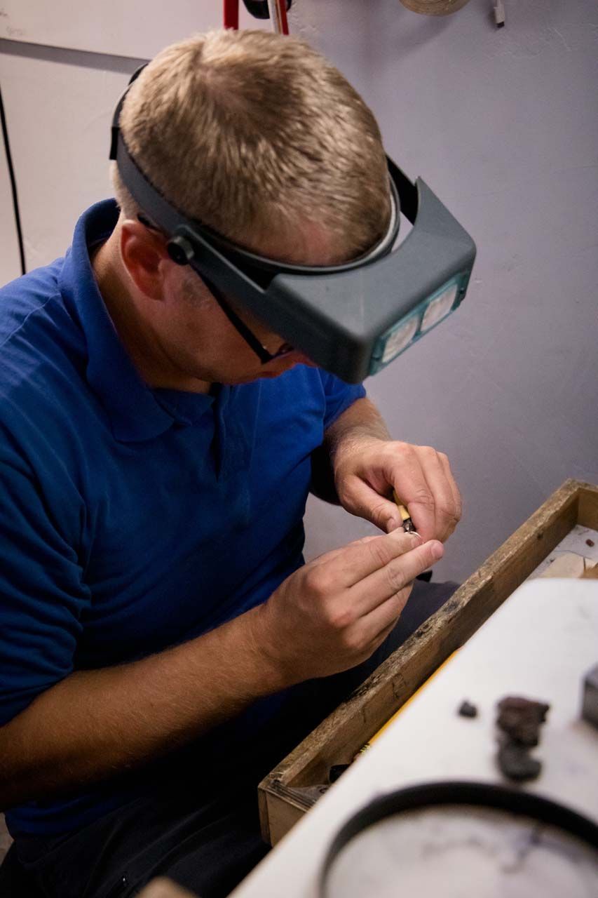 A man wearing a magnifying glass is working on a piece of metal