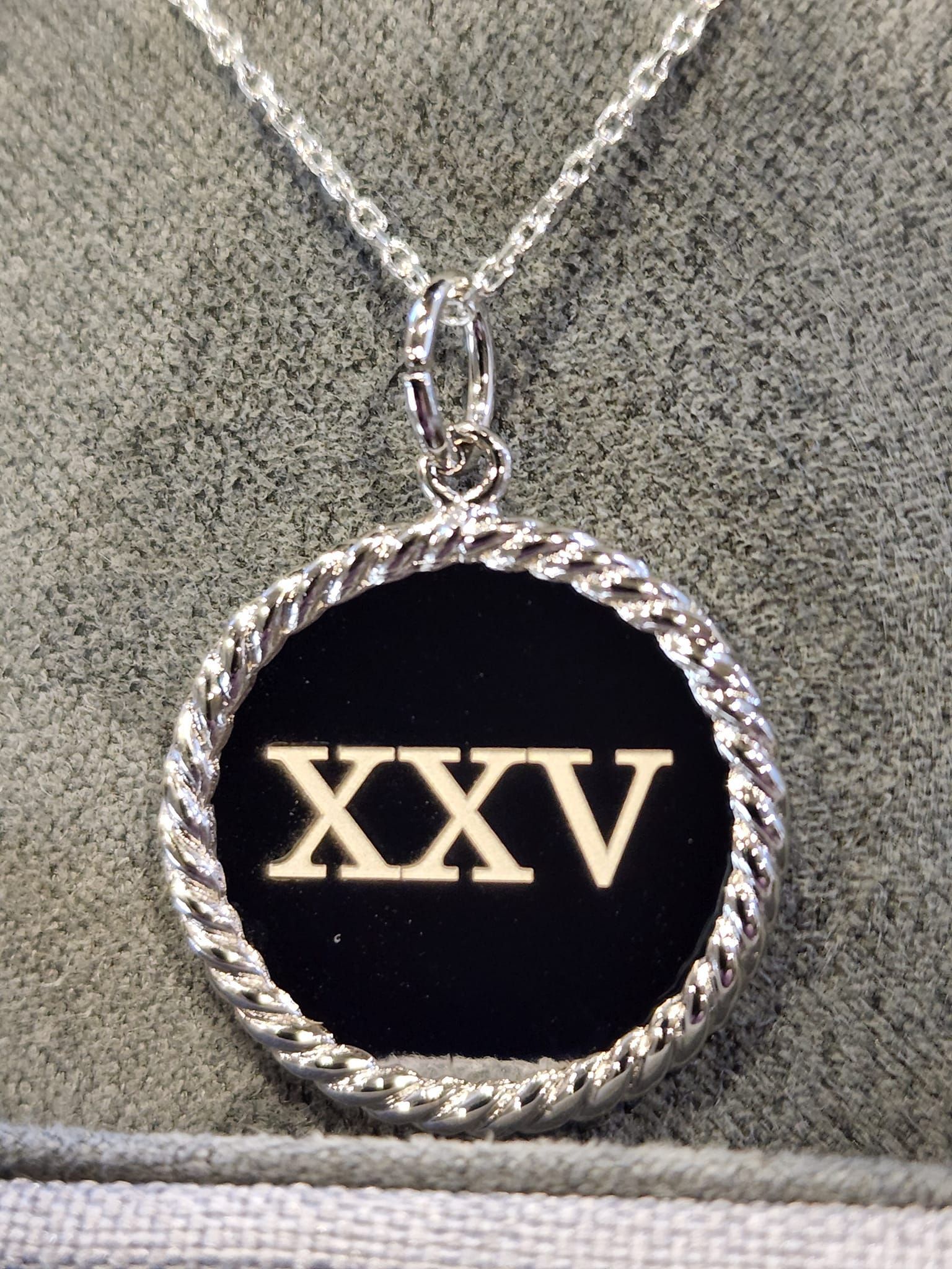 A silver necklace with a black pendant that says xxxv