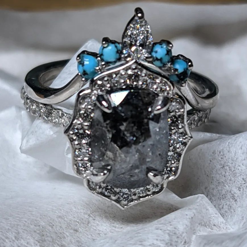 A diamond and turquoise ring is sitting on a white cloth