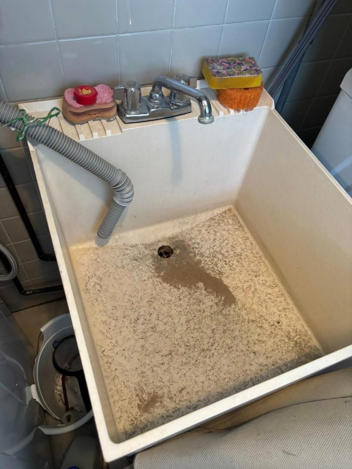 Before cleaning a utility sink with a drain hose, faucet, and cleaning sponges.