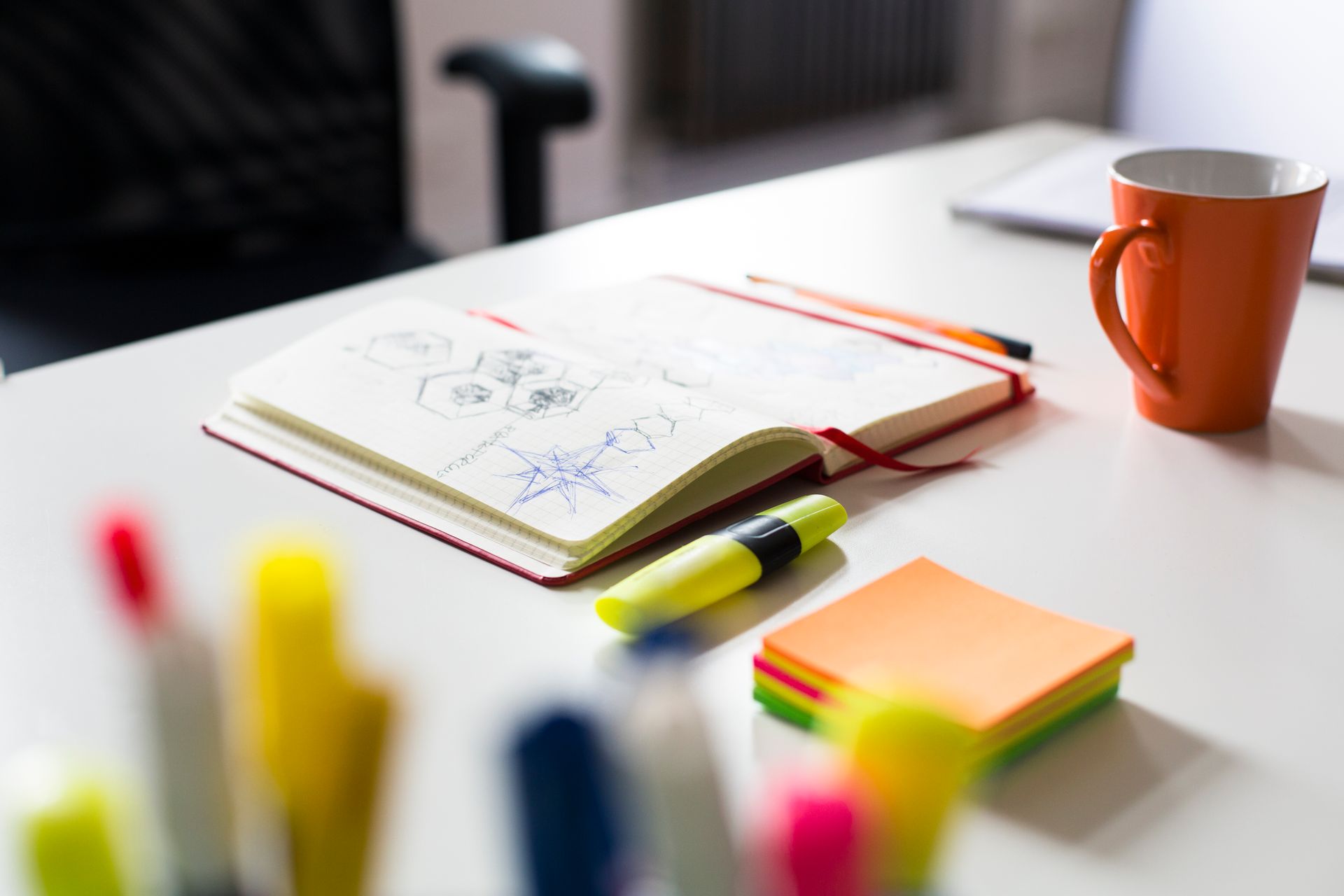 Una scrivania con un quaderno, pennarelli, post-it e una tazza di caffè.