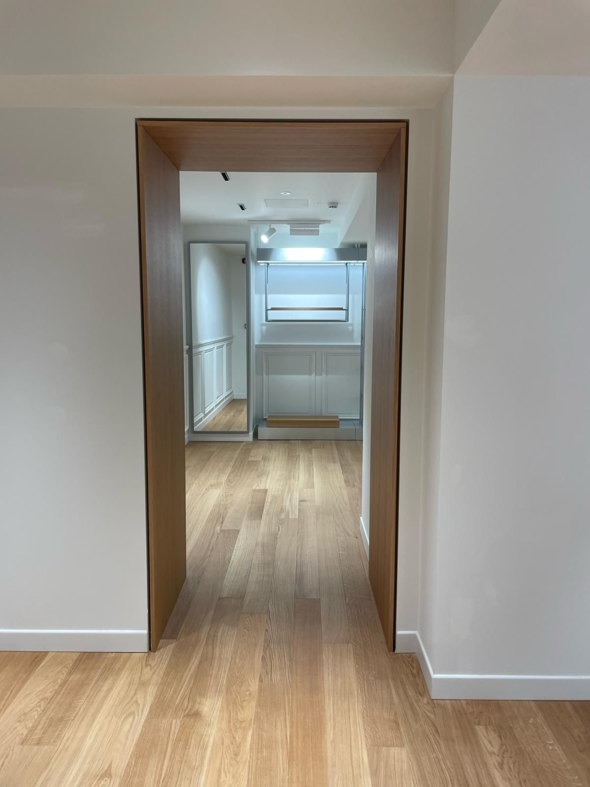 Un corridoio con pavimenti in legno e una porta di legno che conduce a un bagno.