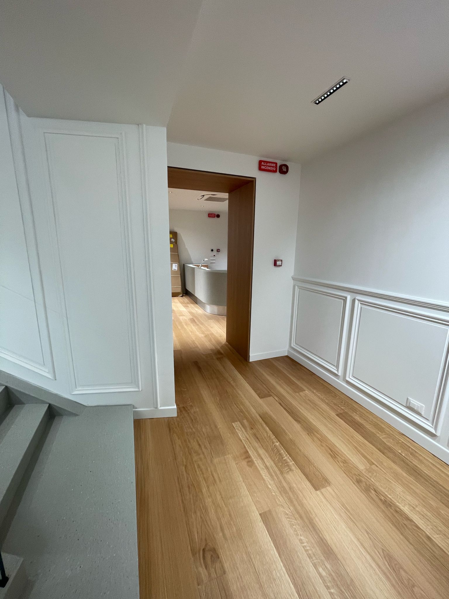 Un corridoio con pavimenti in legno e pareti bianche che conduce a un bagno.