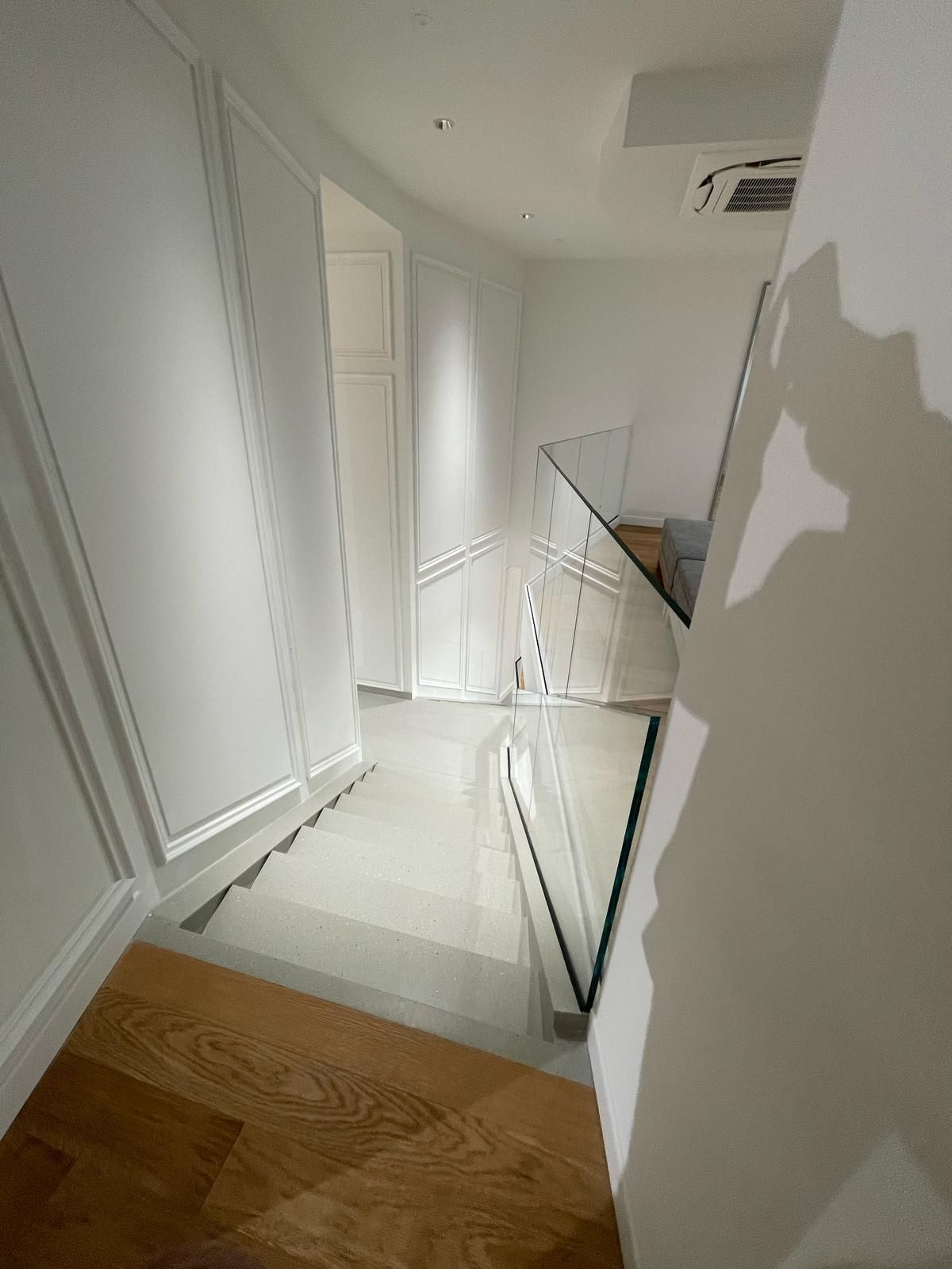 Un corridoio con scale e una ringhiera in vetro in una casa.