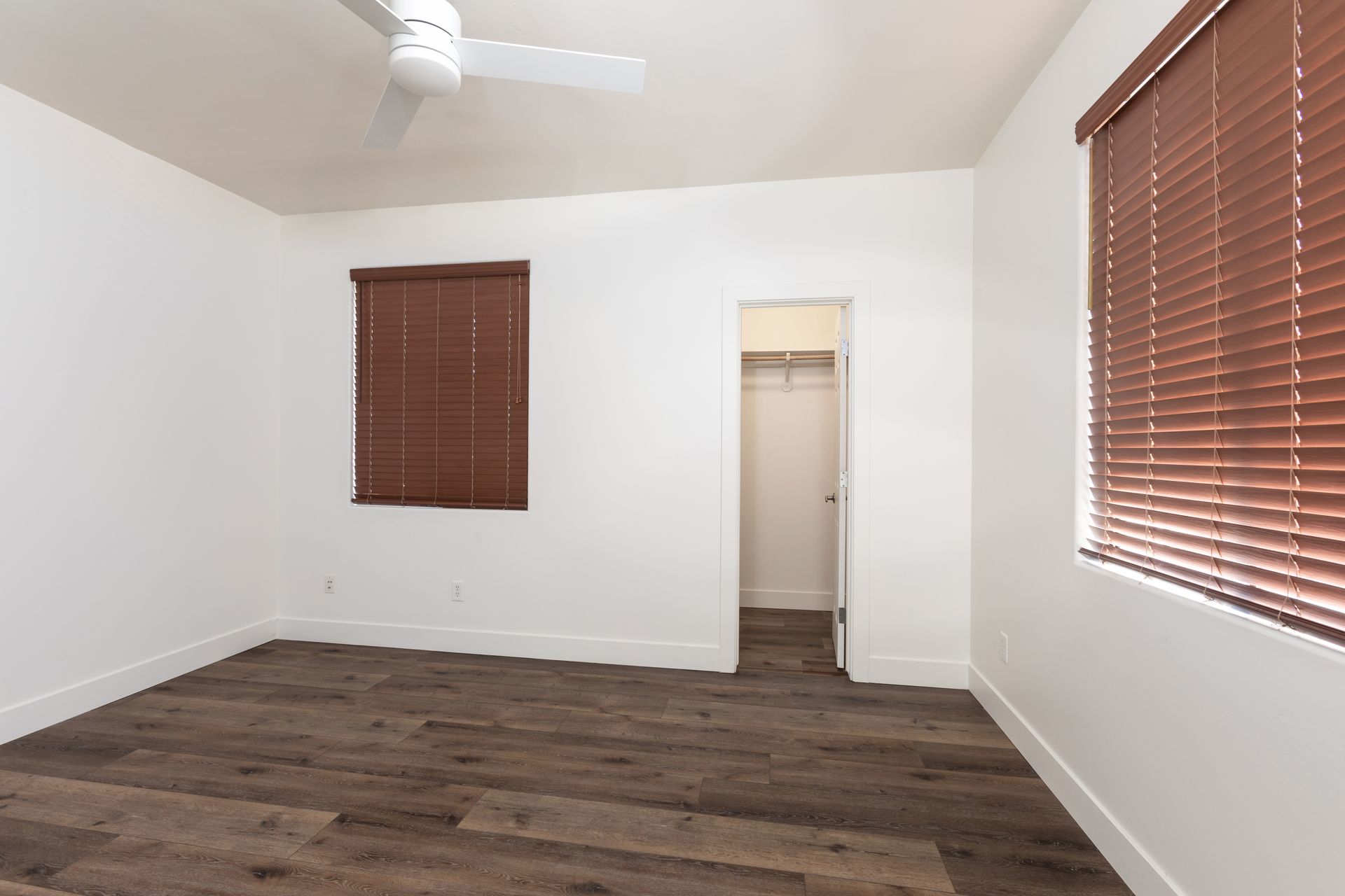 An empty bedroom with a ceiling fan and blinds