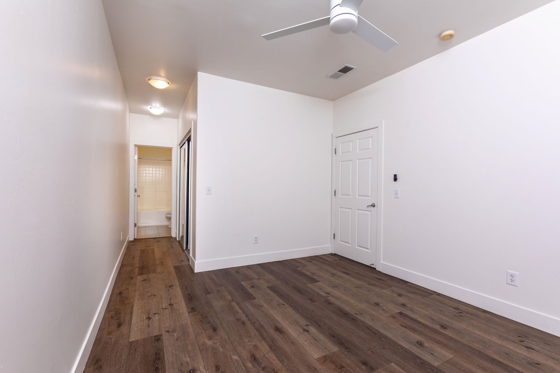 An empty bedroom with hardwood floors and a ceiling fan.