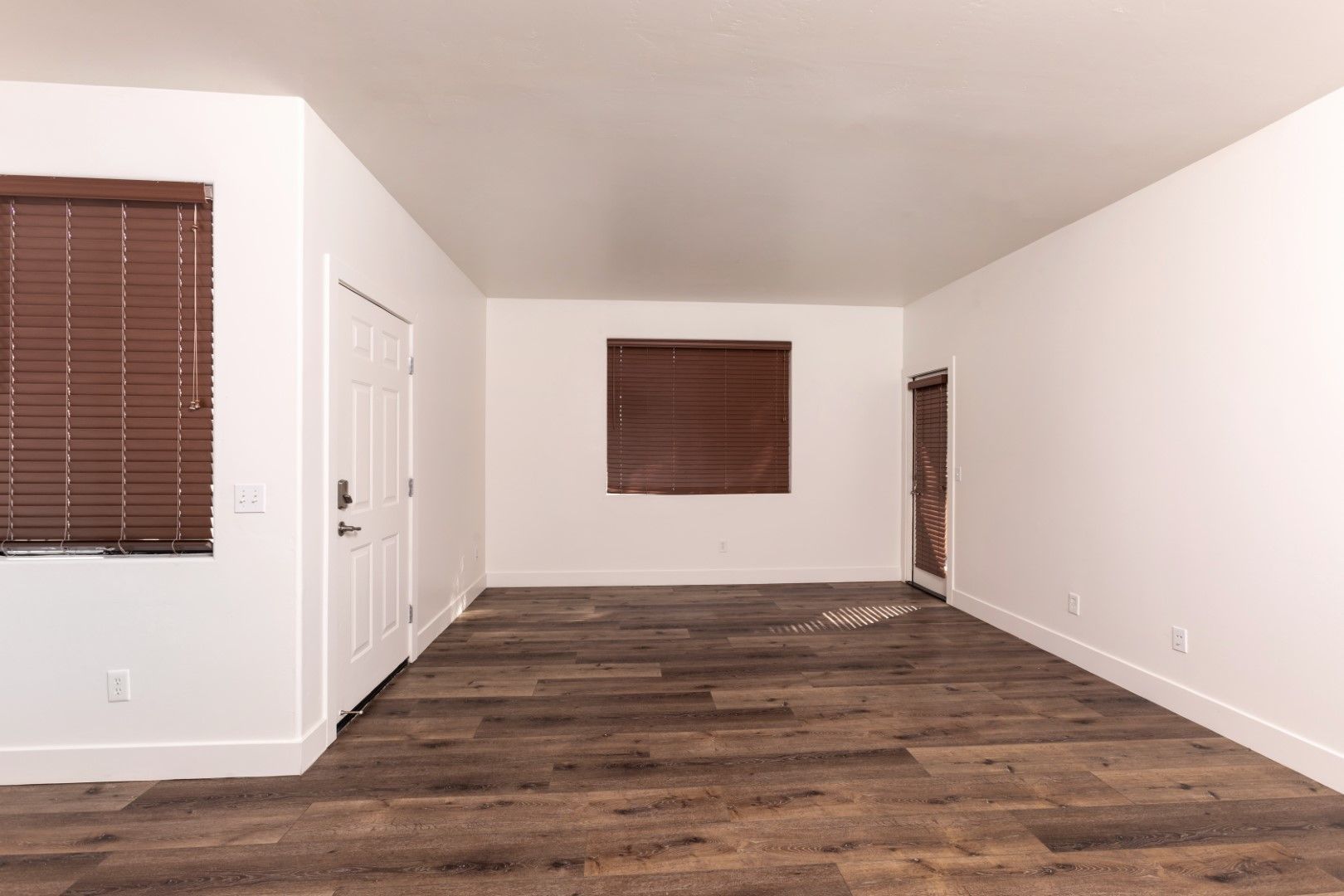 An empty living room with hardwood floors and white walls.