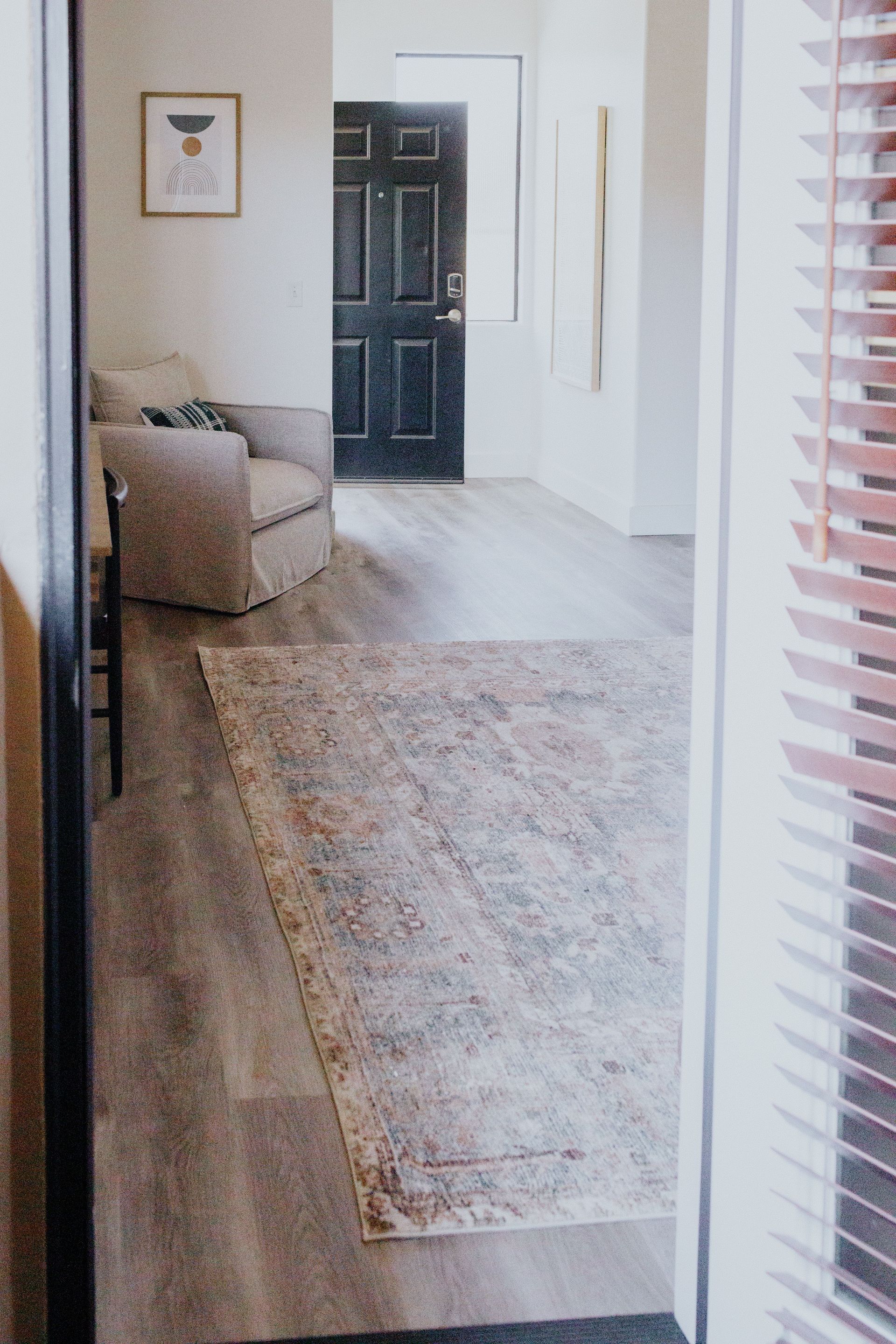 A living room with a rug , chair , and blinds.