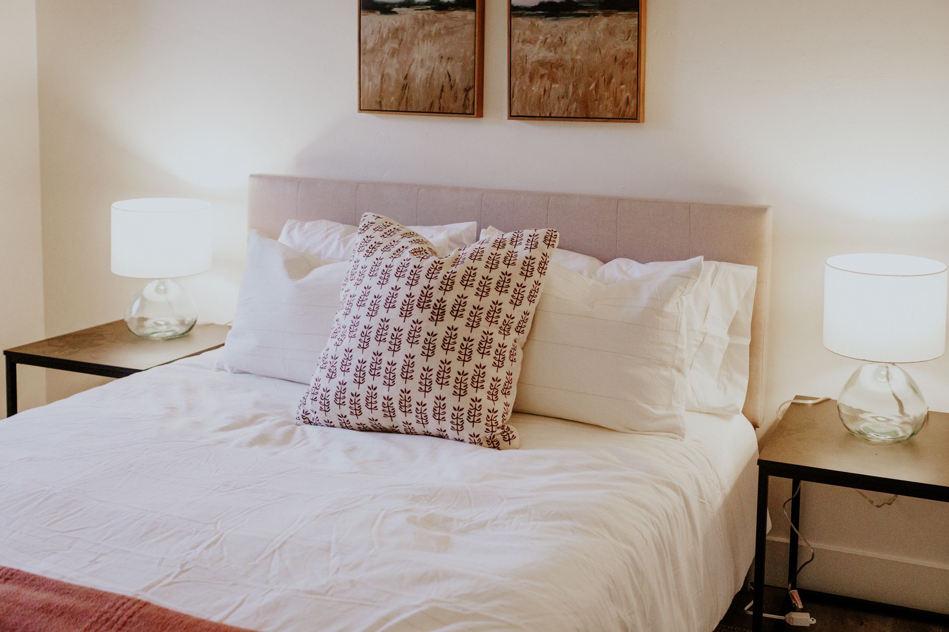 A bedroom with a bed , two nightstands , two lamps and two paintings on the wall.