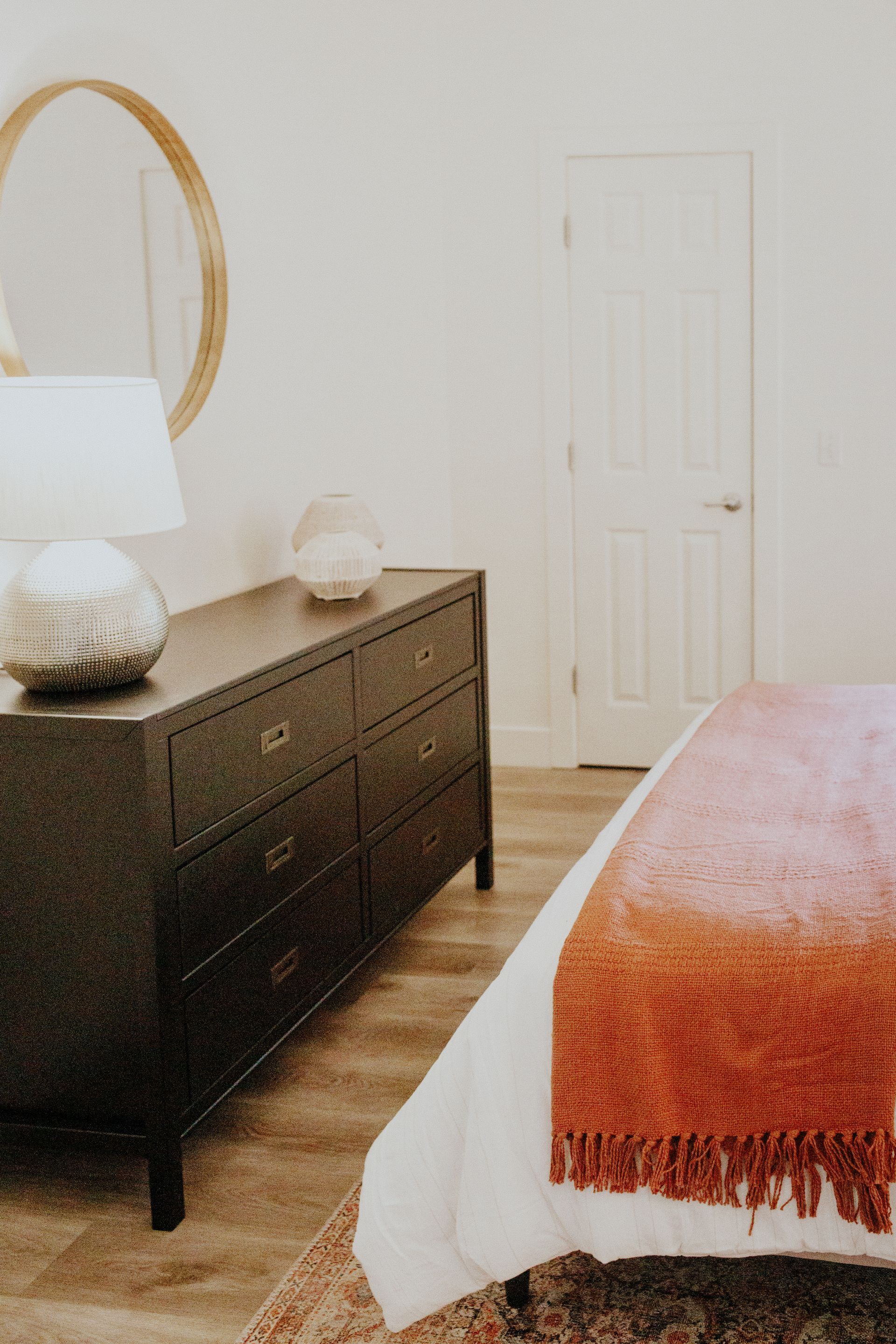 A bedroom with a bed , dresser , lamp and mirror.