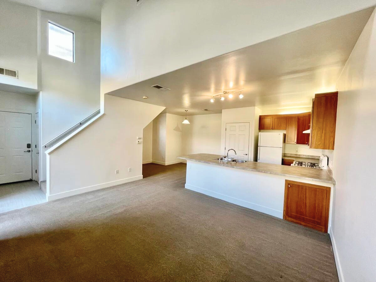 An empty living room with a kitchen and stairs.