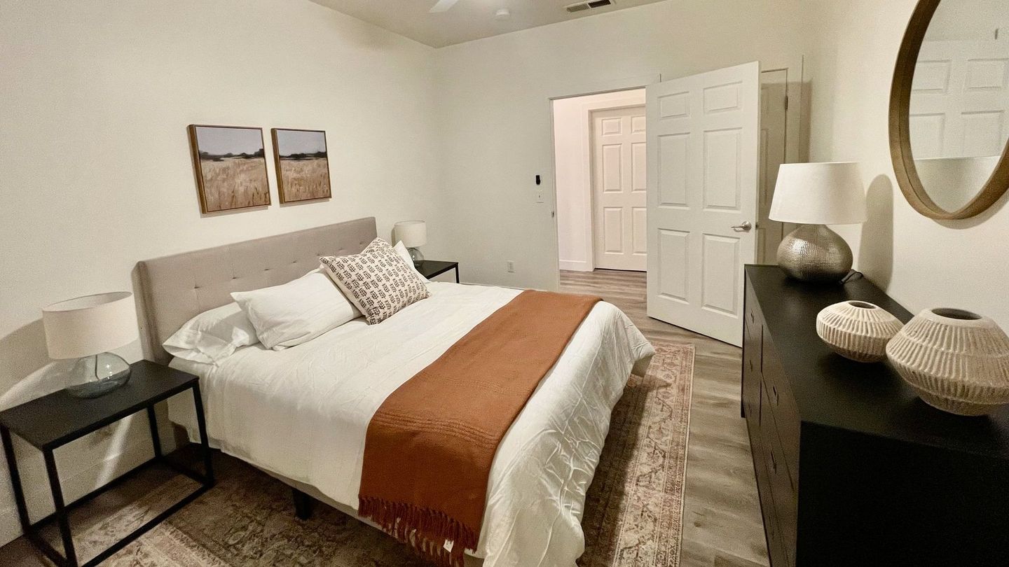 A bedroom with a bed , dresser , nightstand and mirror.