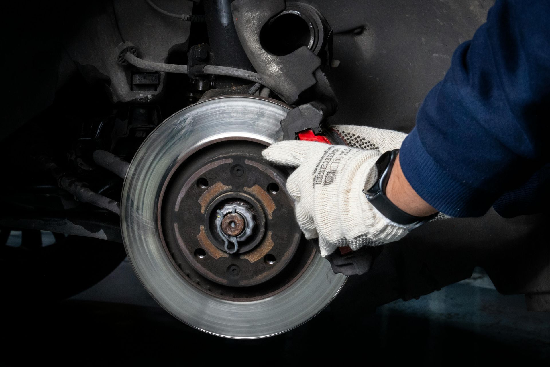 A person in gloves checking a car's brake rotor.